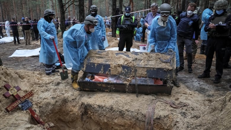 Pekerja darurat mengenakan penutup plastik biru saat mereka menggali massal di situs kuburan hutan Izyum, Ukraina